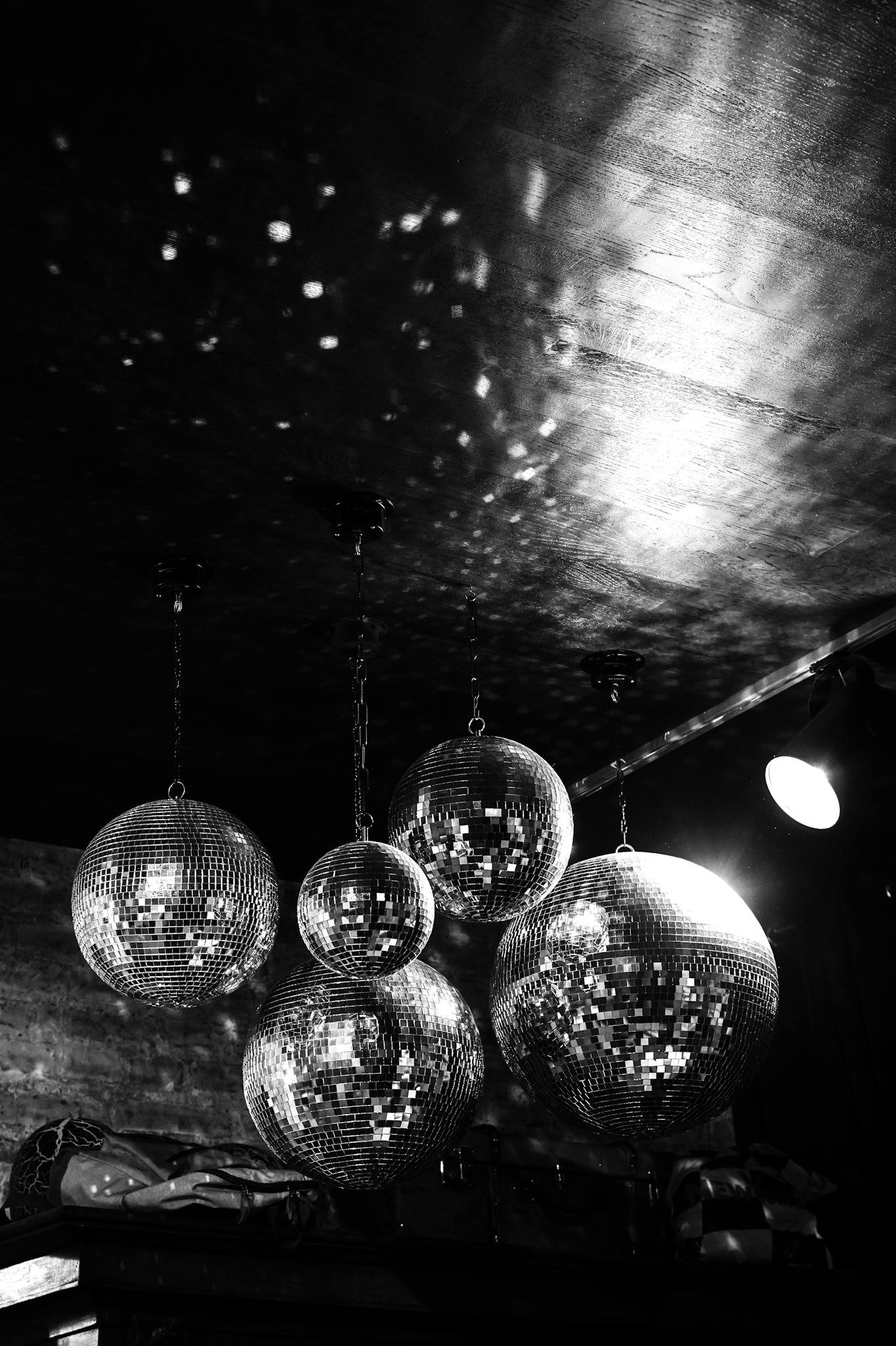 Black and white photo of hanging disco balls reflecting light in a club atmosphere.