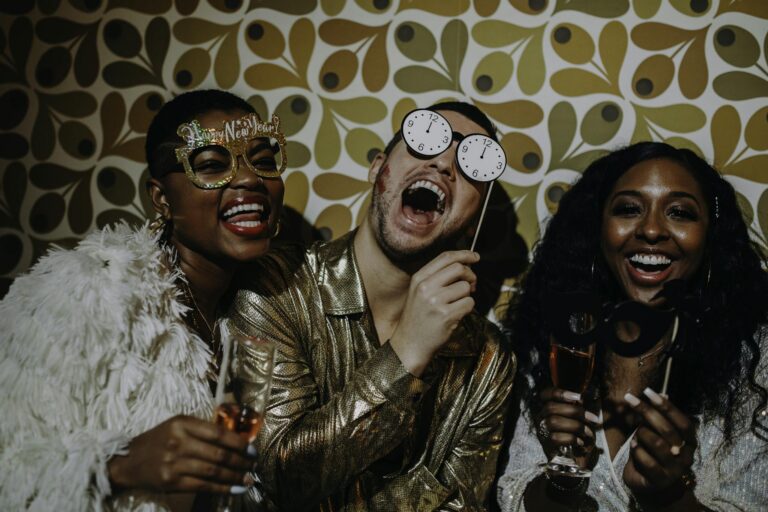 Three friends in festive outfits celebrate New Year's Eve with props and laughter.